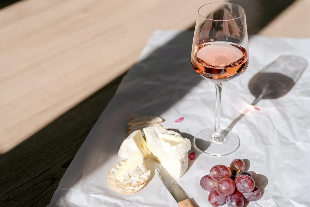A glass of rose wine, cheese, and grapes on a tablecloth