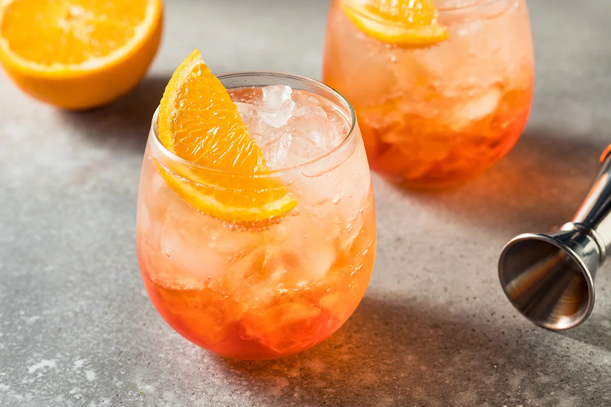 Two glasses of aperol spritz on a counter, next to a sliced orange