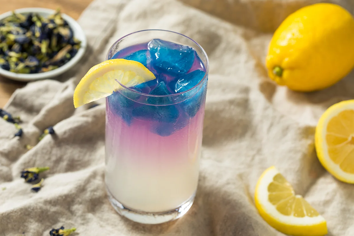 The Bees Knees cocktail with butterfly pea flower, next to a sliced lemon