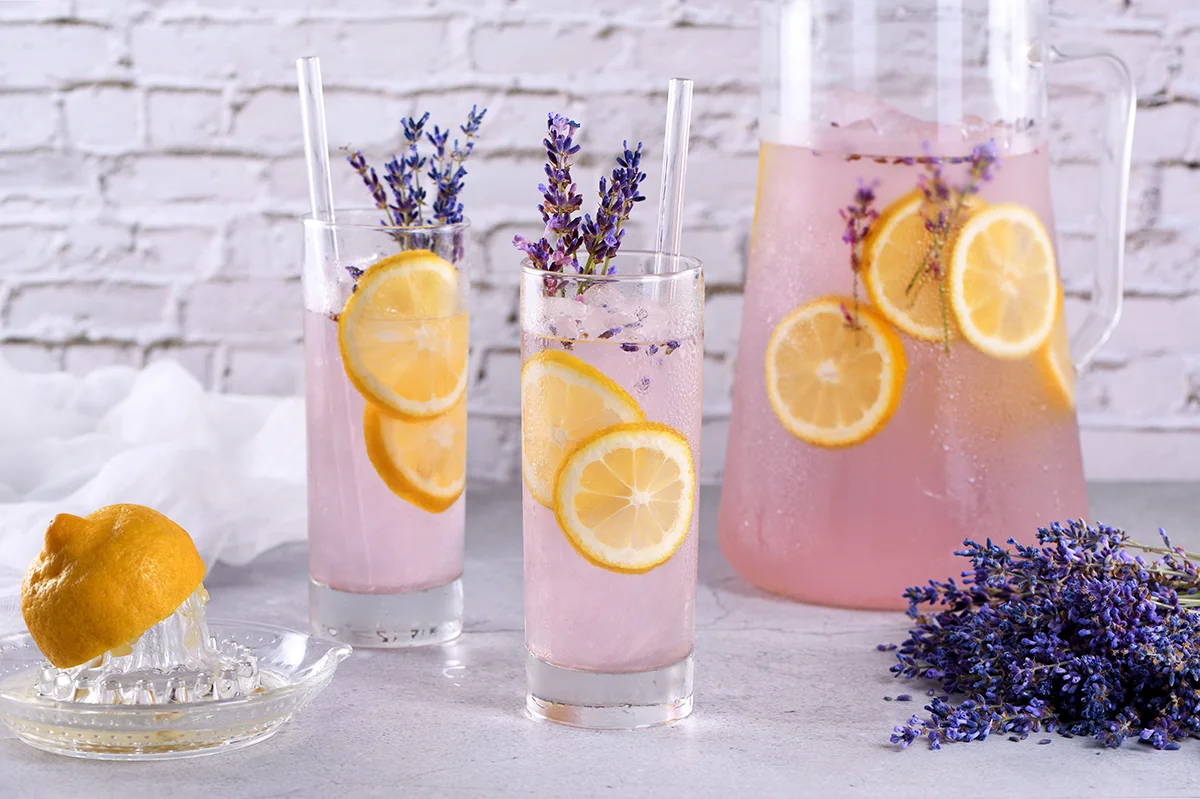 Two lavender lemonade mimosas and a pitcher on a counter