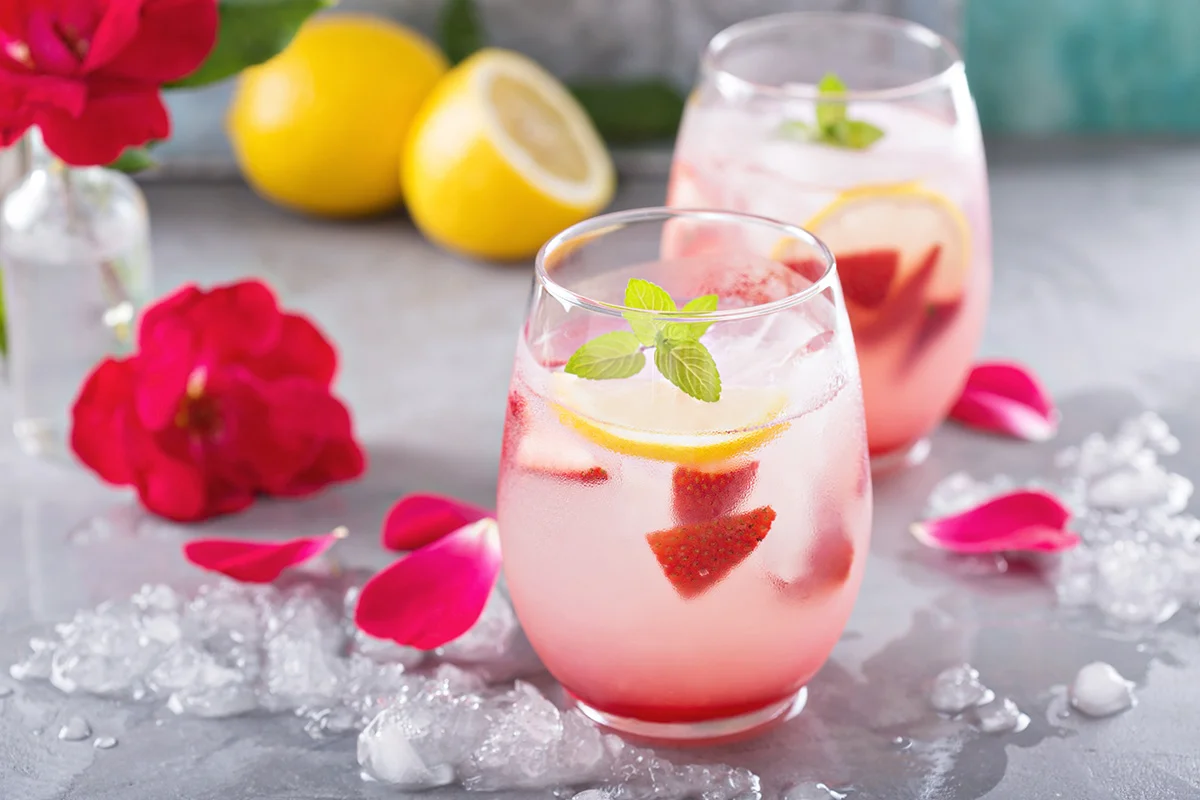 Two glasses of rose sangria, on a table with dark pink flower petals