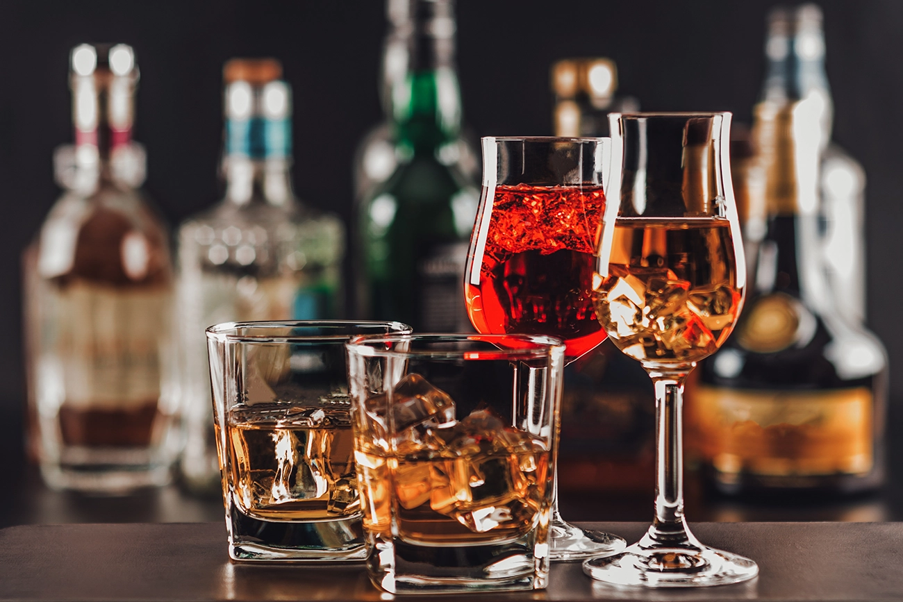Various glasses of red and orange Italian liqueurs, with blurred bottles in the background